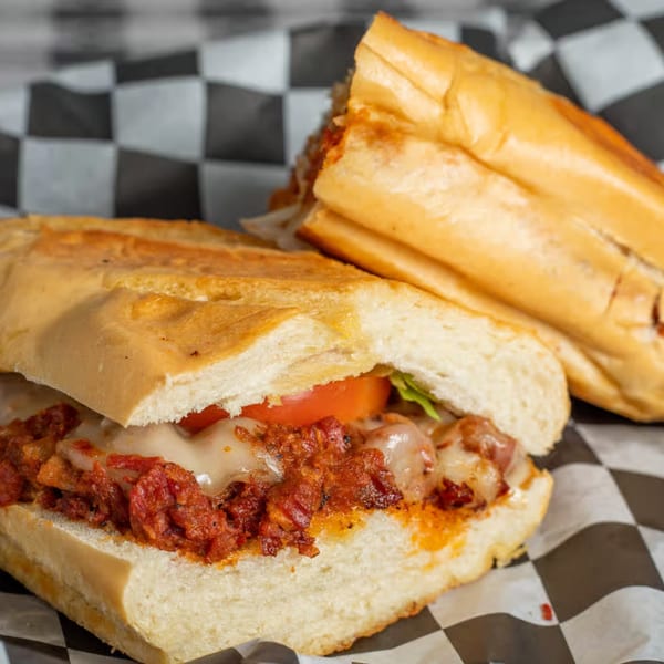 Two Moyitos Cafe & Grill Mexican tortas with melted cheese, meat, tomato, and lettuce on checkered paper.