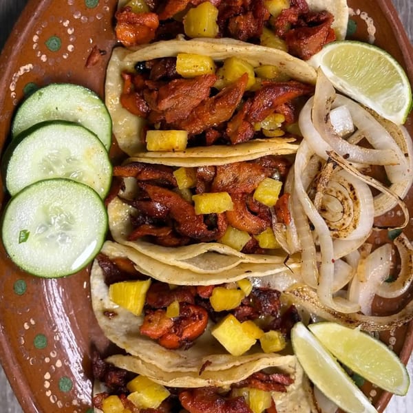 Moyitos Cafe & Grill's al pastor tacos with pineapple, grilled onions, cucumbers, and lime wedges.