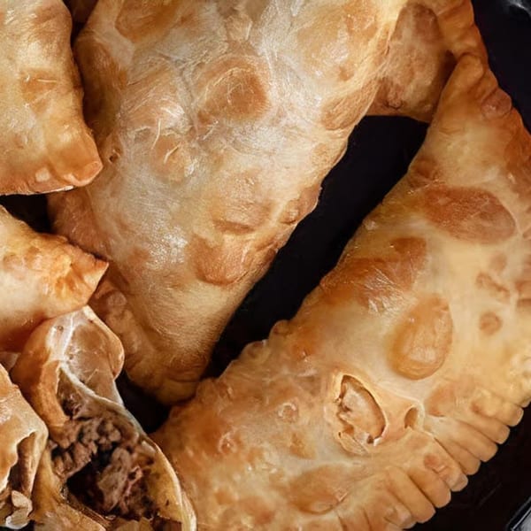 Close-up of several golden-brown Moyitos Cafe & Grill empanadas, one revealing a savory meat filling.