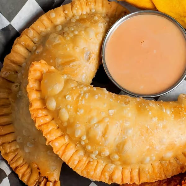 Two golden-brown Moyitos Cafe & Grill empanadas with a side of creamy dipping sauce.